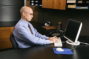 Caucasian middle-aged businessman sitting at desk in office typing on computer.
