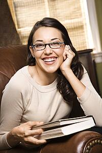 Caucasian/Hispanic young woman sitting in leather chair holding book and smiling at viewer.