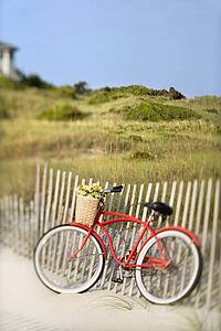 Red vintage bicycle with basket and flowers leaning against wooden fence at beach.