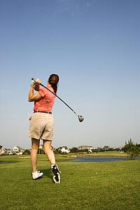Back view of Caucasion mid-adult woman swinging golf club.