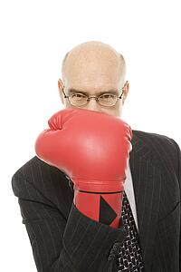 Caucasian middle-aged man holding up hand with red boxing glove up to face.