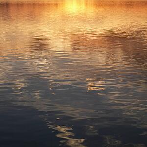 Reflections of orange and yellow sunset on water.