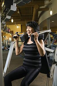 Mature Asian adult female using exercise machine at gym.