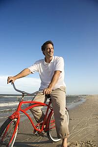 Caucasian mid-adult man posing on bicycle on beach.