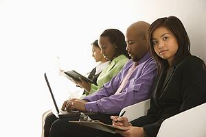 Vietnamese businesswoman sitting with clipboard looking at viewer with others in background.