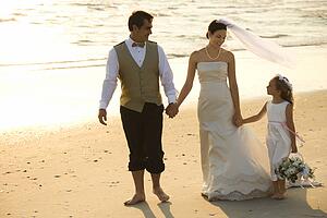 Bride and groom with flower girl walking barefoot on beach