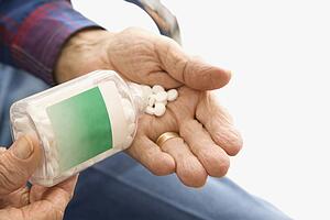 Close-up of elderly male Caucasio pouring pills into hand.