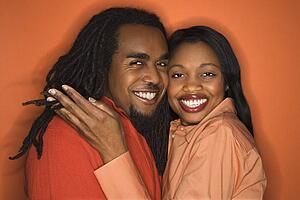 Smiling African-American mid-adult couple wearing orange clothing on orange background.