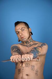 Barechested Caucasian mid-adult man with tattoos and piercings holding knife.