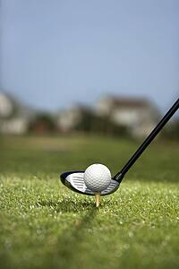 Image of golf ball on tee with golf club behind ball.