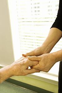 Caucasian female nurse massaging arthritic hands of elderly man at retirement community center.
