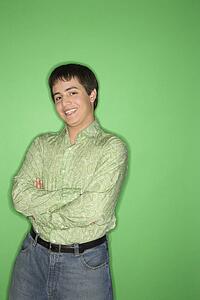 Portrait of Caucasian teen boy smiling with crossed arms standing against green background. l