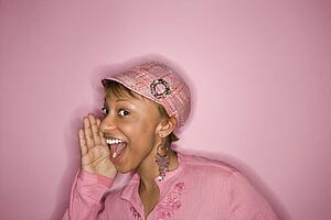 Portrait of smiling young African-American adult woman on pink background yelling and smiling at unseen person.