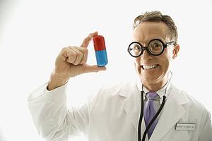Mid-adult Caucasian male doctor wearing eyeglasses holding an oversized medical pill.