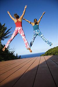 Caucasian mid-adult women jumping into air with arms and legs outstretched.