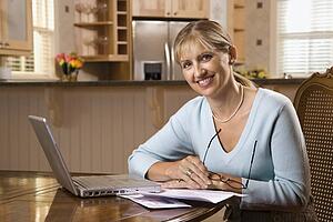 Caucasian mid-adult woman paying bills on laptop computer looking at viewer and smiling.