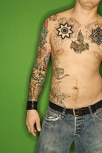 Bare torso of Caucasian man with tattoos standing against green background.