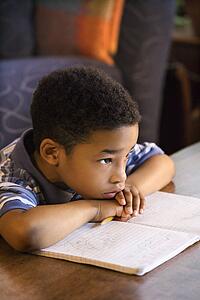 Portrait of young boy with head on arms with book in front.