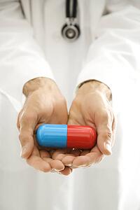Mid-adult Caucasian male doctor holding out an oversized medical pill.