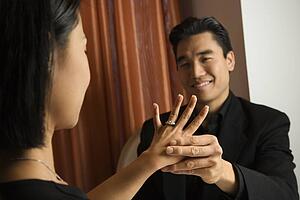 Prime adult Asian female admiring engagement ring with male in background.