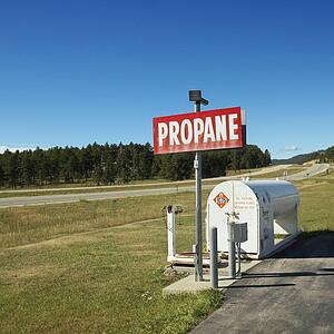 Propane tank with sign on side of rural road.