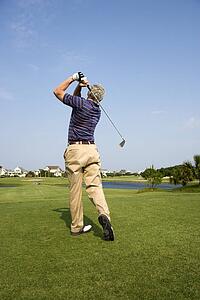 Back view of Caucasion mid-adult man swinging golf club.
