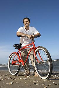 Caucasian mid-adult man posing with red bicycle on beach.