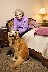 Elderly Caucasian woman and dog in her bedroom at retirement community center.