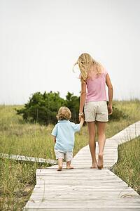 Caucasian pre-teen girl walking on beach access walkway and holding hands with Caucasian male toddler.
