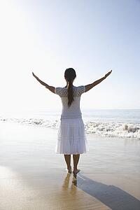 Young Asian female holding arms up standing at the shoreline.