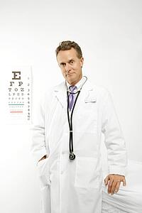 Mid-adult Caucasian male doctor with eye chart in background.