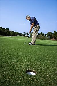 Image of mid-adult male putting golf ball with hole in foreground.