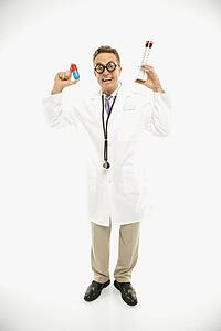 Mid-adult Caucasian male doctor wearing eyeglasses holding an oversized medical pill and syringe.