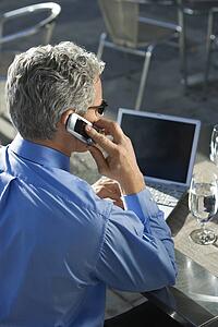Rear view of prime adult Caucasian man in suit talking on cellphone and looking at laptop.