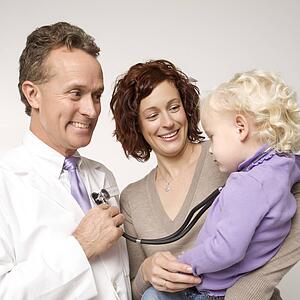 Caucasian female toddler with stethoscope around her neck as middle-aged male doctor holds it to his chest.