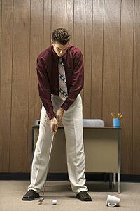 Caucasion mid-adult retro businessman putting golf ball into coffee cup in his office.