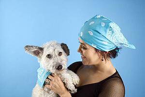 Hispanic mid-adult woman holding small white dog wearing matching bandanas.