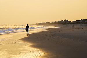 Caucasian pre-teen boy walking sihouette on beach at sunset.