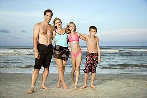 Caucasian family of four standing on beach.