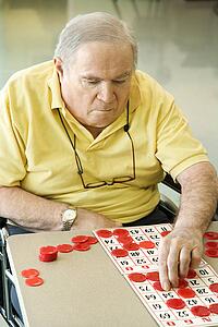 Elderly Caucasian man sitting in wheelchair playing bingo at retirement community center.