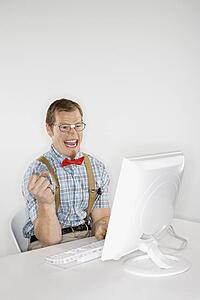 Caucasian young man dressed like nerd excited looking at computer monitor.