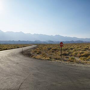 Road with stop sign in barren landscape with mountain in distance.
