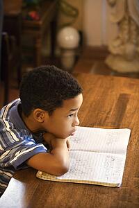 Portrait of young boy with head on arms with book in front.