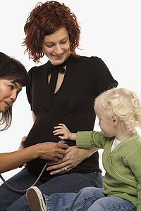 Nurse holding stethoscope on Caucasian pregnant woman's belly.