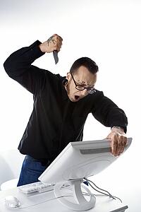 Caucasian mid-adult man with tattoos and piercings stabbing computer with knife.