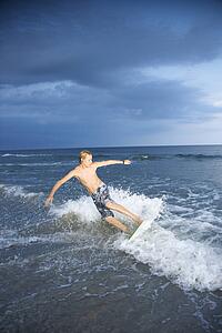 Caucasian male teen riding skimboard.