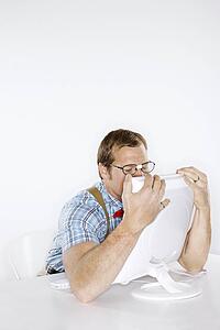 Caucasian young man dressed like nerd embracing computer with face pressed to monitor.