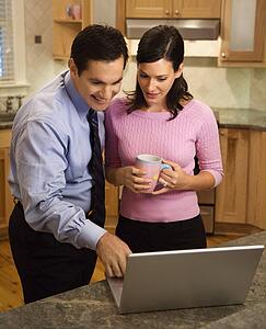 Mid-adult couple looking at laptop computer while standing in kitchen.