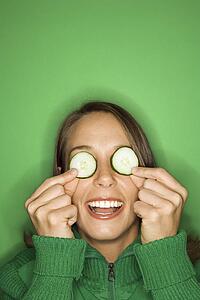 Portrait of young adult Caucasian woman on green background holding cucumber slices over her eyes.