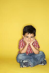 Filipino male child sitting with head on hands.